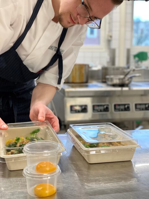 kock som lägger upp mat i lådor för take away