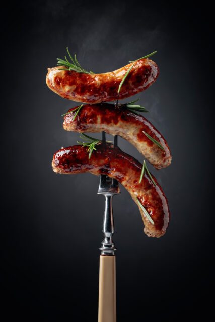 Grilled Bavarian sausages with rosemary. tre bayerska korvar spättade på ett grillspett med rosemarin överst